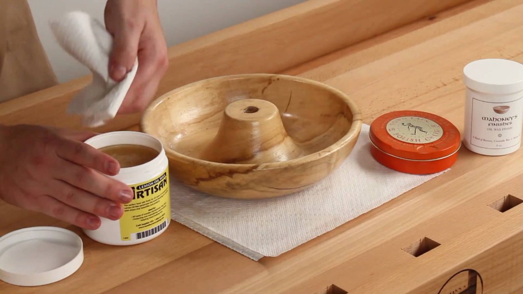 Applying lemon oil wax to a turned nutcracker bowl with a soft cloth.