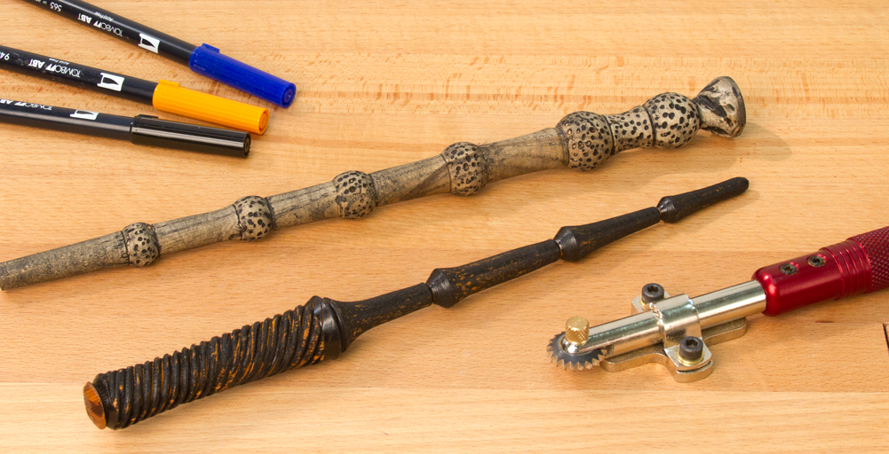 Two turned magic wands laid on a table with a texturing tool and several colored markers.