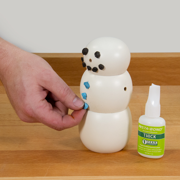 Gluing buttons on the snowman with CA glue.