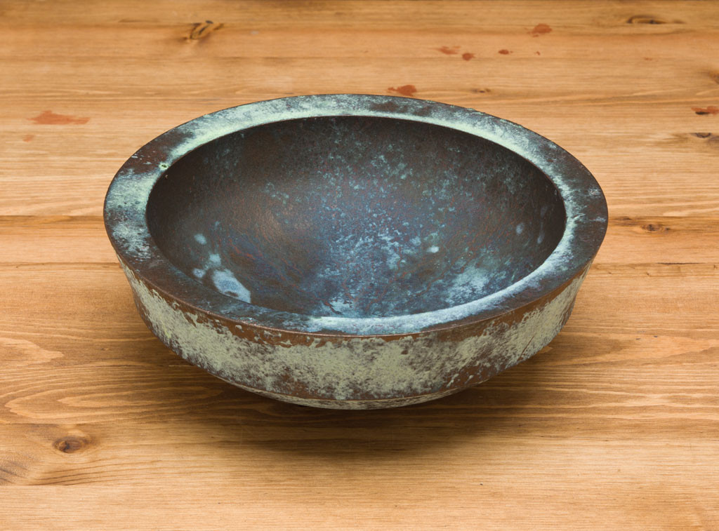 A wood bowl with bronze paint and green patina.