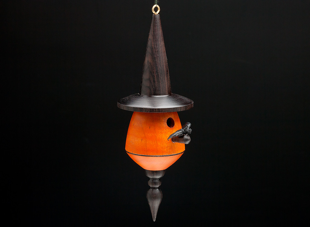 A turned bat house ornament with orange body and black hat and finial.