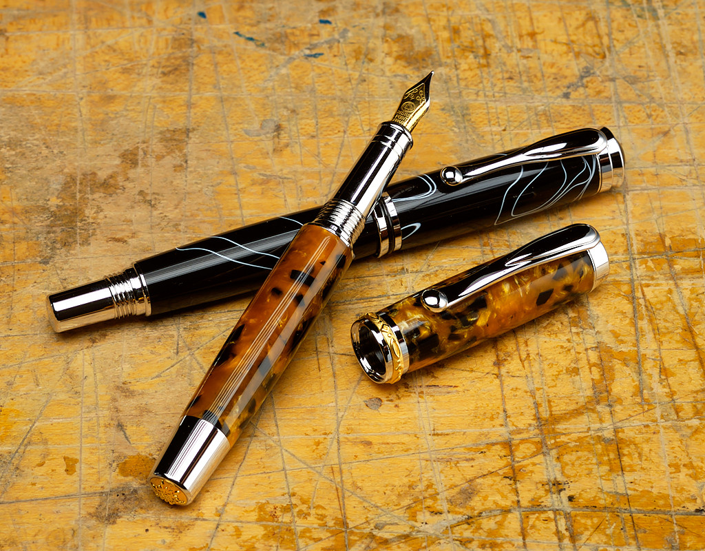 Two turned fountain pens displayed on a workbench.