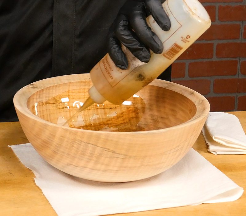 Pouring walnut oil finish onto bowl.